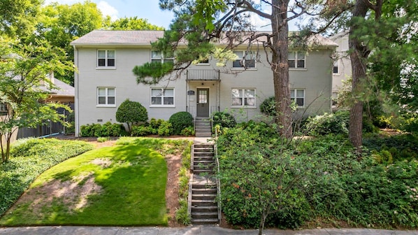 A two-story residential building with a front entrance, a small front yard, and a staircase leading to the entrance. - Brookwood Courtyard by BCA Furnished Apartments Bcc1b 01 A (Atlanta)