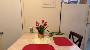 Une table à manger recouverte d’une nappe blanche, agrémentée de sets de table rouges et d’un vase de tulipes rouges.