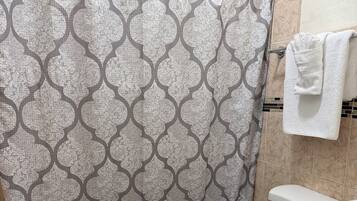 Een badkamer met een gordijn met een patroon, een toilet, een wastafel met een handdoek en een badmat.