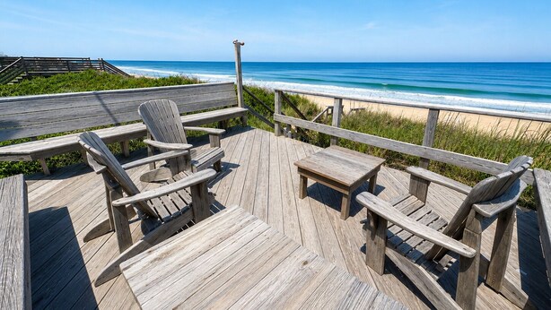 A wooden deck with chairs and a table overlooking a beach. - Anderson's Tranquility - Classic Oceanfront 3 BR Cottage in Southern Shores (Southern Shores)