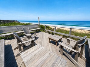 Une terrasse en bois avec des chaises et une table, donnant sur une plage.