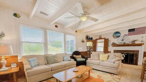 A living room with two sofas, a coffee table, a fireplace, and a ceiling fan. - Anderson's Tranquility - Classic Oceanfront 3 BR Cottage in Southern Shores (Southern Shores)