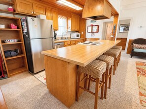 Eine kompakte Küche mit Holzschnitzschränken, einem Edelstahl-Kühlschrank, einer Mikrowelle und einer Bar mit einem Sitzhocker.