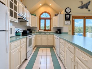 A kitchen with white cabinets, a teal countertop, a window with a view, and a clock on the wall. - Mariah - 3 BR home, 400 yards to the beach in Southern Shores (Southern Shores)