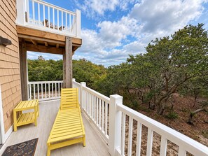 A wooden deck with a white railing, a yellow bench, and a view of a forested area. - Mariah - 3 BR home, 400 yards to the beach in Southern Shores (Southern Shores)