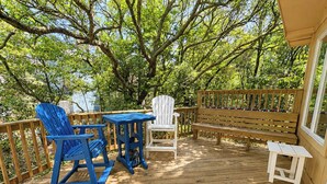 A wooden deck with a table and two chairs, surrounded by trees. - Sea Gables -  Oceanside 3 BR home on Private Wooded Lot (Southern Shores)