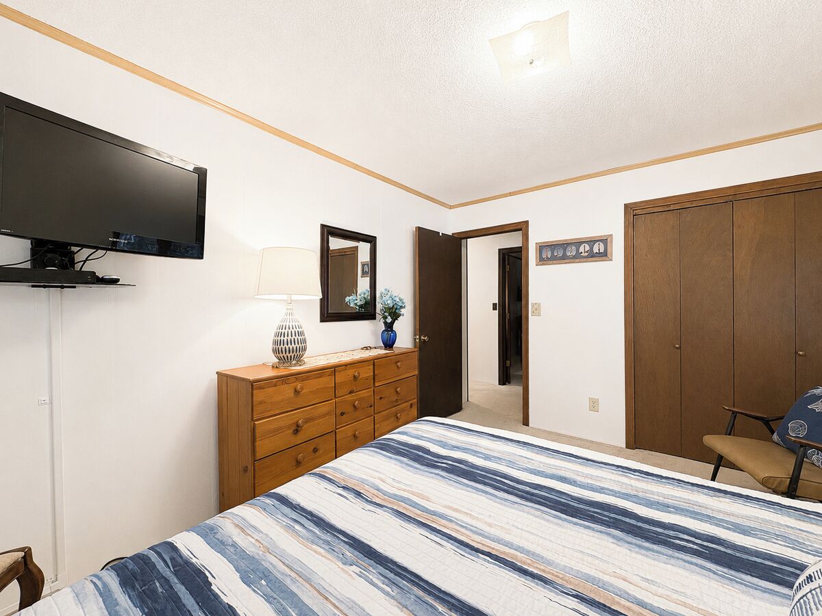 A bedroom with a bed, a dresser, a television, a mirror, and a wardrobe.