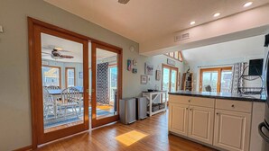 A spacious kitchen with wooden flooring, a dining area with white chairs, and a sliding glass door leading to an outdoor patio. - Salty Paws - 4 BR Oceanside vacation home in the heart of Duck w/Private Pool (Duck)