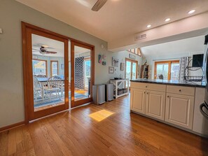 A spacious kitchen with wooden flooring, a dining area with white chairs, and a sliding glass door leading to an outdoor patio. - Salty Paws - 4 BR Oceanside vacation home in the heart of Duck w/Private Pool (Duck)