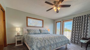 A bedroom with a bed, a nightstand, a ceiling fan, a window with blinds, and a view of the outdoors. - Salty Paws - 4 BR Oceanside vacation home in the heart of Duck w/Private Pool (Duck)