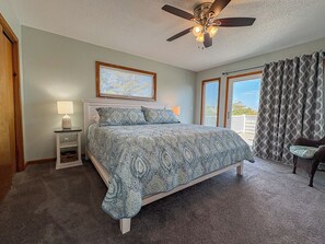 A bedroom with a bed, a nightstand, a ceiling fan, a window with blinds, and a view of the outdoors. - Salty Paws - 4 BR Oceanside vacation home in the heart of Duck w/Private Pool (Duck)