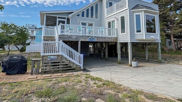 A two-story house with a covered porch, a staircase, and a sign indicating 'Salty Paws'. - Salty Paws - 4 BR Oceanside vacation home in the heart of Duck w/Private Pool (Duck)