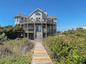 A two-story house with a balcony and a wooden pathway leading to the entrance. - Twinscape - 5 BR Oceanfront Escape w/Community Pool/Tennis (Duck)