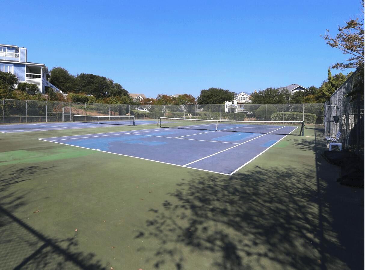 Una cancha de tenis con una red, rodeada por una cerca y árboles.