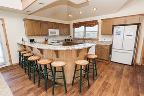 A kitchen with a central island, wooden cabinets, a refrigerator, and bar stools. - Twinscape - 5 BR Oceanfront Escape w/Community Pool/Tennis (Duck)