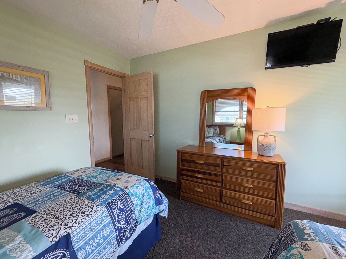 A bedroom with a bed, a dresser, a mirror, a television, and a door.