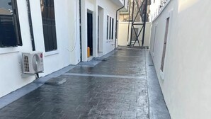 Un couloir étroit, dallé et revêtu d’un sol carrelé, avec des murs blancs et un escalier en métal noir.