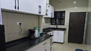 Une cuisine moderne avec des armoires blanches, un plan de travail noir et un pare-feu en carreaux. On y trouve une cuisinière, un évier et une fenêtre au-dessus de l’évier.