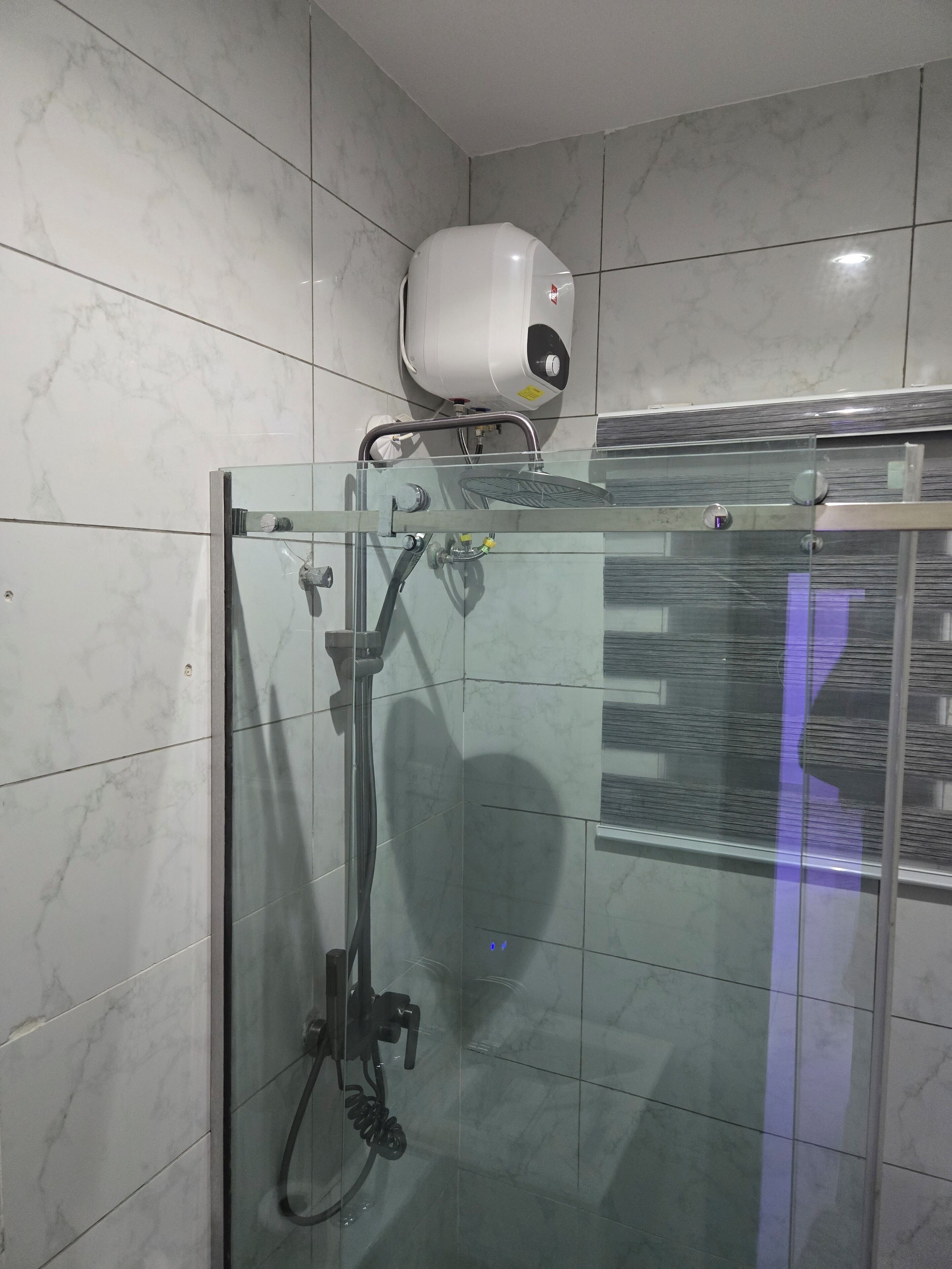 A glass-enclosed shower with a handheld showerhead and a wall-mounted water heater.