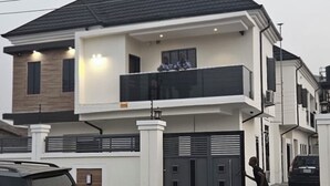 Une maison à deux étages avec un balcon, une entrée fermée par un portail et une voiture garée devant.