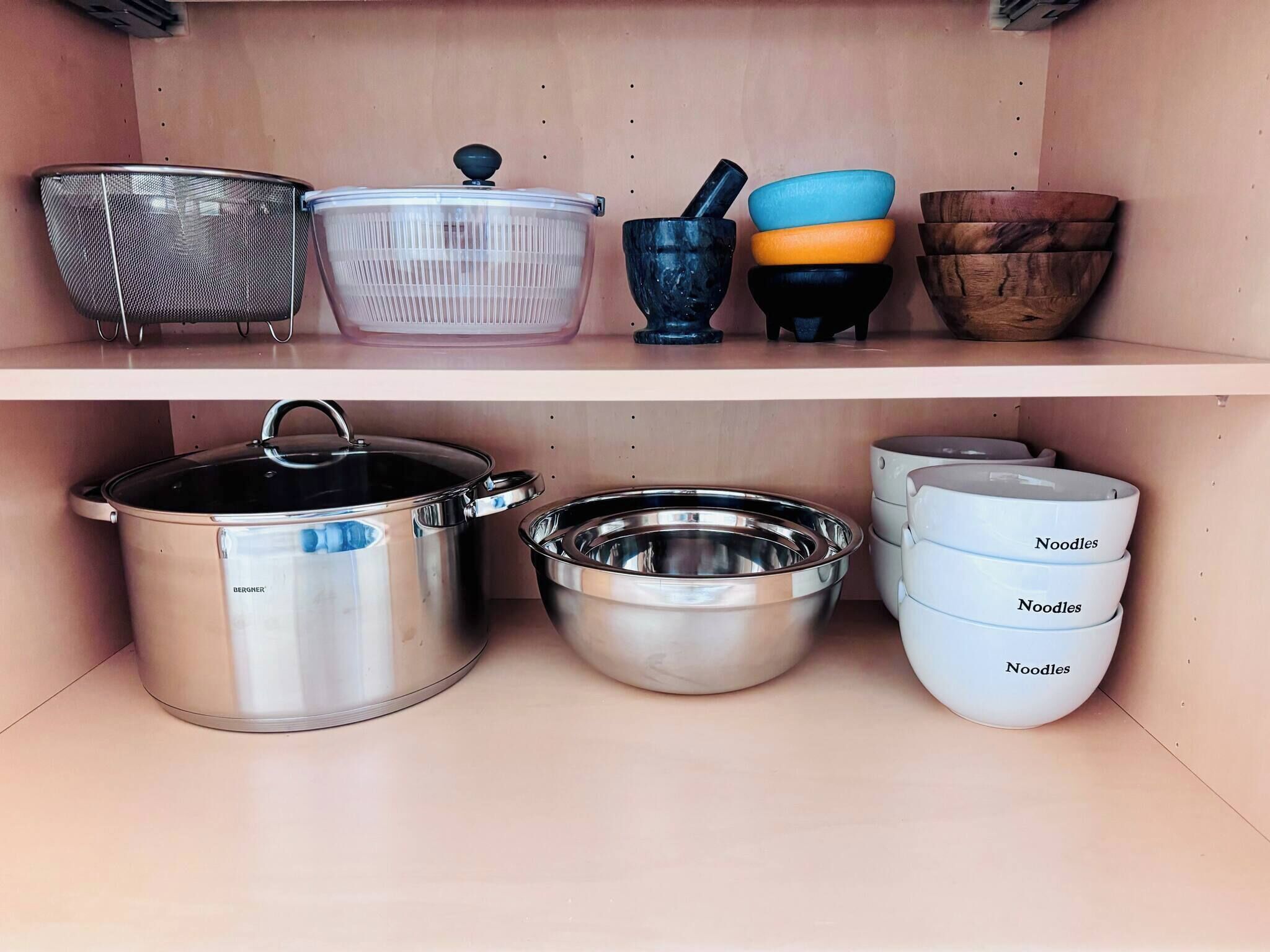 A kitchen shelf with various utensils and cookware, including a strainer, colander, and pots.