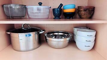 A kitchen shelf with various utensils and cookware, including a strainer, colander, and pots.