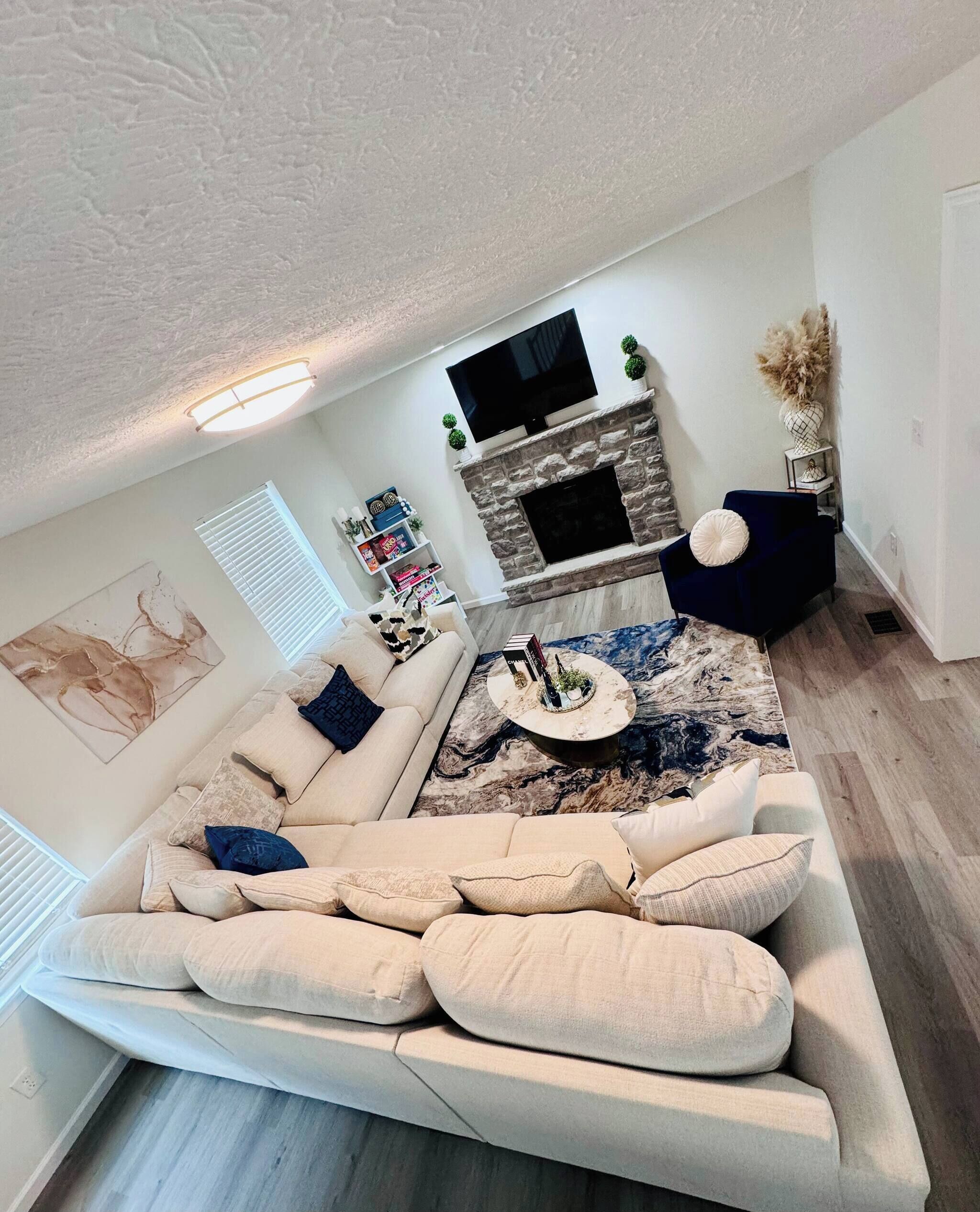 Un salon moderne avec un grand canapé, un téléviseur à écran plat fixé au-dessus d’une cheminée en pierre et un vase décoratif.