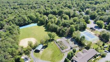 Vue aérienne d’un quartier résidentiel avec un grand espace vert, un court de tennis et un bâtiment doté d’un toit en pente.