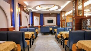 A restaurant with booths and tables, a central TV screen, and decorative wall panels. - Hotel Roopali (Jabalpur)