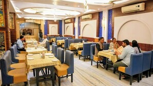 A restaurant with multiple tables and chairs, air conditioning units, and a ceiling fan. - Hotel Roopali (Jabalpur)