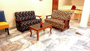 A living room with patterned sofas, a glass-top coffee table, and a decorative vase. - Hotel Roopali (Jabalpur)