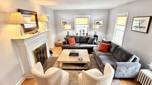 A living room with a fireplace, grey sofas, a coffee table, and two armchairs. - Beautiful home in Burlington's South End, humans and dogs welcome! (Burlington)