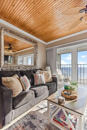 A living room with a dark gray sofa, a large mirror, and a coffee table with a basket and books. - Oceanfront Comfort at the Cabana! (Carolina Beach)