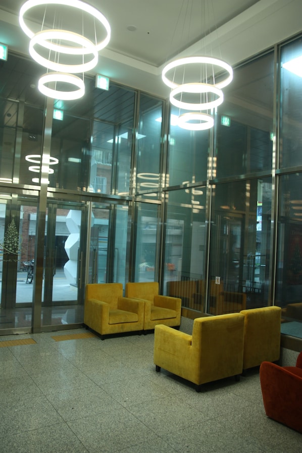 A modern lobby with glass walls, yellow and red seating, and circular ceiling lights.