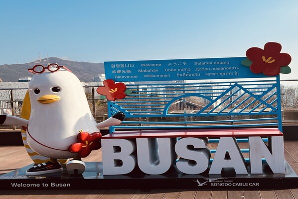 Un letrero de bienvenida con un personaje promocional y la palabra 'BUSAN' destacada.