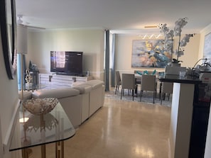 A modern living room with a flat-screen TV, a glass coffee table, a sofa, and a dining area with chairs and a table. - THE COASTAL ! GREAT 2BD 2BA APT WITH STUNNING VIEWS AT AVENTURA YACHT CLUB ! (Aventura)