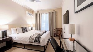 Une chambre d’hôtel équipée d’un lit, de tables de chevet, d’une chaise, d’un bureau, d’un ventilateur de plafond et d’un téléviseur fixé au mur.