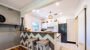 Une cuisine moderne avec un coin bar, deux tabourets, un réfrigérateur et une fenêtre.