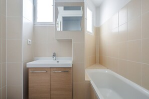 Ein Badezimmer mit einem weißen Waschbecken, Holzschränken, einem Spiegel und einer Badewanne.