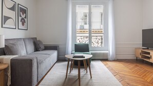 A modern living room with a grey sofa, a small round table, a green armchair, and a TV stand. - Blueground | Saint-Philippe-du-Roule, view, nr Arc de Triomphe (Paris)