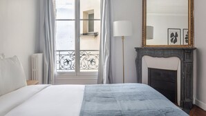 A bedroom with a bed, a fireplace, a mirror, and a view of the outside. - Blueground | Saint-Philippe-du-Roule, view, nr Arc de Triomphe (Paris)