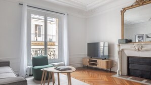 A modern living room with a sofa, a green armchair, a TV on a wooden stand, a fireplace, and a large mirror. - Blueground | Saint-Philippe-du-Roule, view, nr Arc de Triomphe (Paris)
