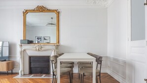 A dining area with a white table and four chairs, a fireplace, and a large mirror on the wall. - Blueground | Saint-Philippe-du-Roule, view, nr Arc de Triomphe (Paris)