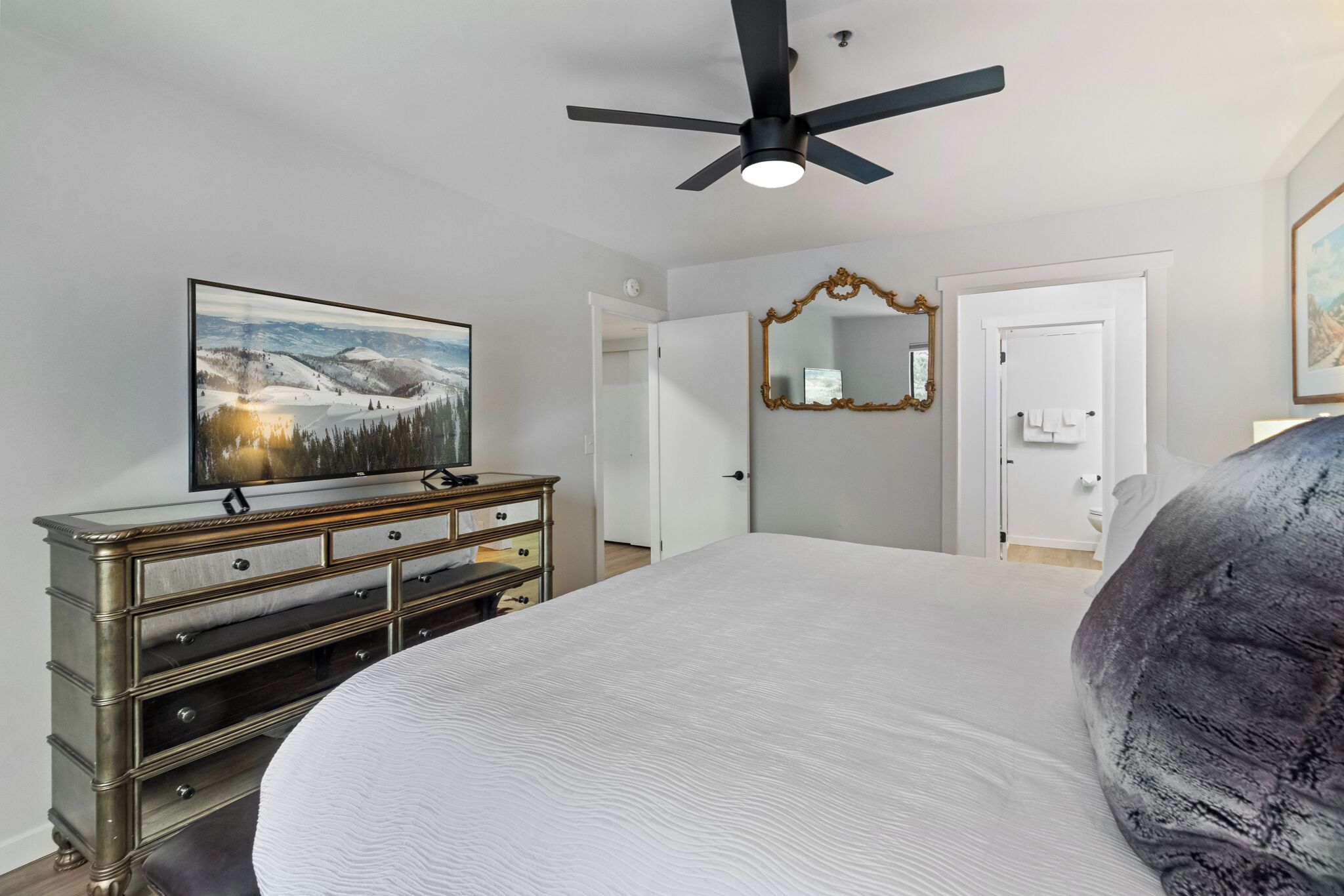 Una camera da letto con un letto, una cassettiera, una ventola a soffitto e un quadro appeso al muro.