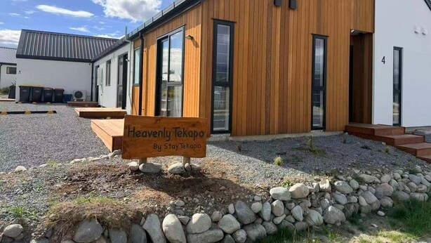 Un edificio moderno con fachada de madera y ventanas grandes, identificado como "Heavenly Tekapo By StayTekapo".