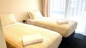 Dos camas individuales con ropa de cama a rayas, una mesita de noche y una ventana con cortinas translúcidas.