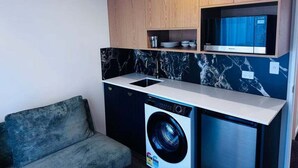 Una cocina compacta con lavadora, microondas y un pequeño estante con vajilla.