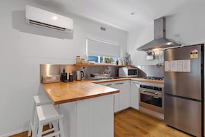 Una cocina moderna con armarios blancos, encimera de madera, electrodomésticos de acero inoxidable y ventana con vistas a palmeras.