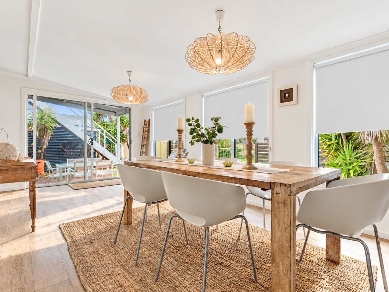 A dining area with a wooden table, white chairs, and a woven rug.
