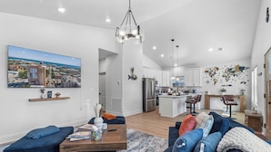 A modern living room with a large window, a dining area, and a kitchen. - Pelican Landing At The Bay (Pensacola)